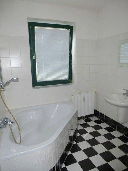 Badezimmer mit Eckbadewanne, Waschbecken und Fenster, gefliest in Schwarz-Weiß.