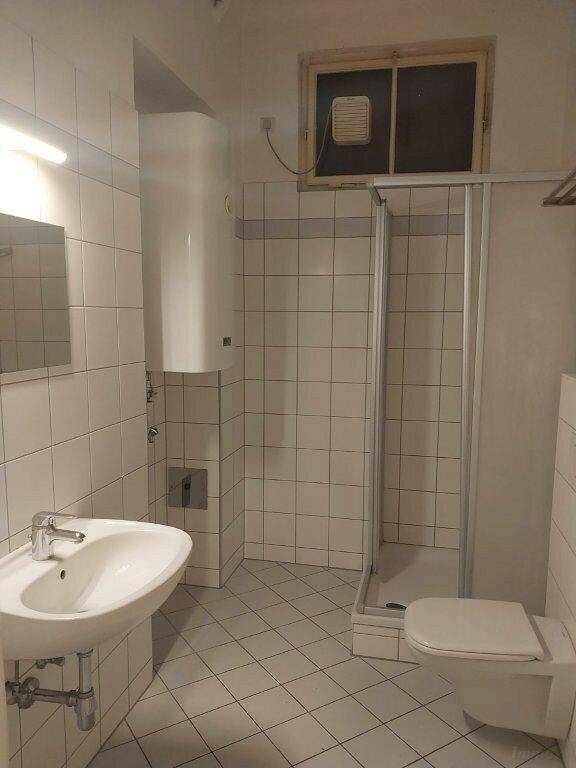 Funktionales Badezimmer mit weißen Fliesen, Dusche, WC und Waschbecken.