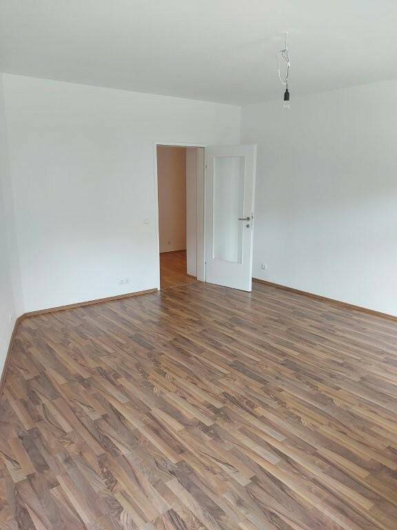 Geräumiger, unmöblierter Raum mit weißen Wänden und einem Laminatboden in Holzoptik.