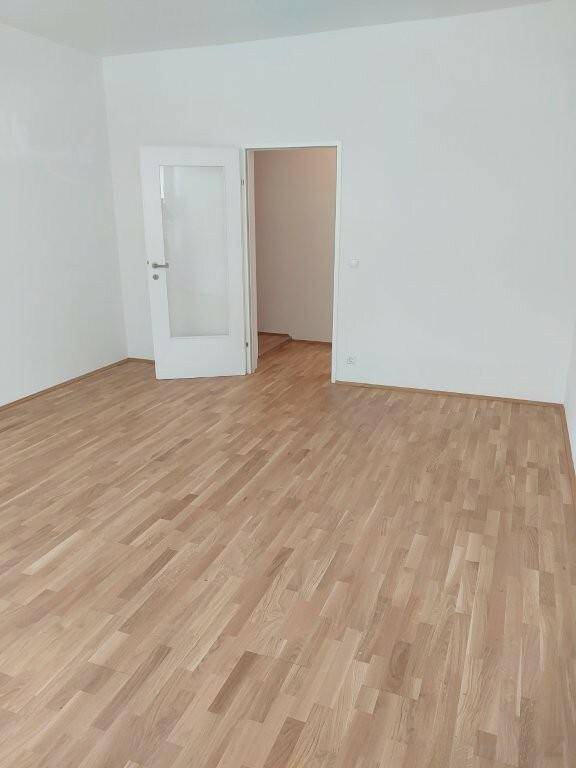 Heller, leerer Raum mit weiß gestrichenen Wänden und hellem Holzparkettboden.
