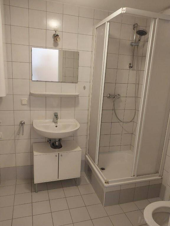 Funktionales Badezimmer mit Duschkabine, Waschbecken und weißen Fliesen.