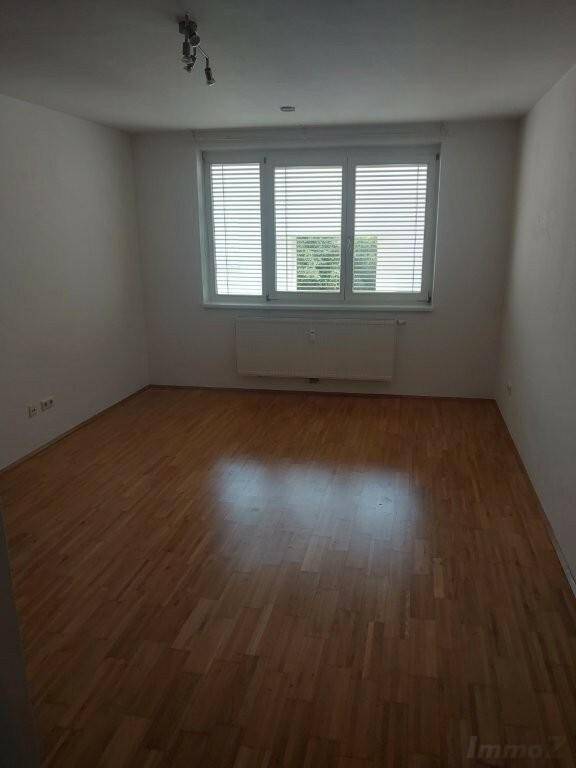 Helles Zimmer mit Laminatboden und Fenster mit Jalousien, ideal als Schlafzimmer.