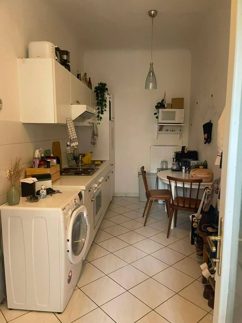 Schmale Küche mit weißen Schränken, Fliesenboden und Essbereich.