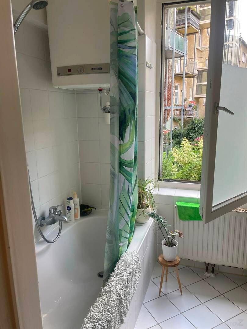 Badezimmer mit Badewanne, Duschvorhang und Fenster zum Garten.