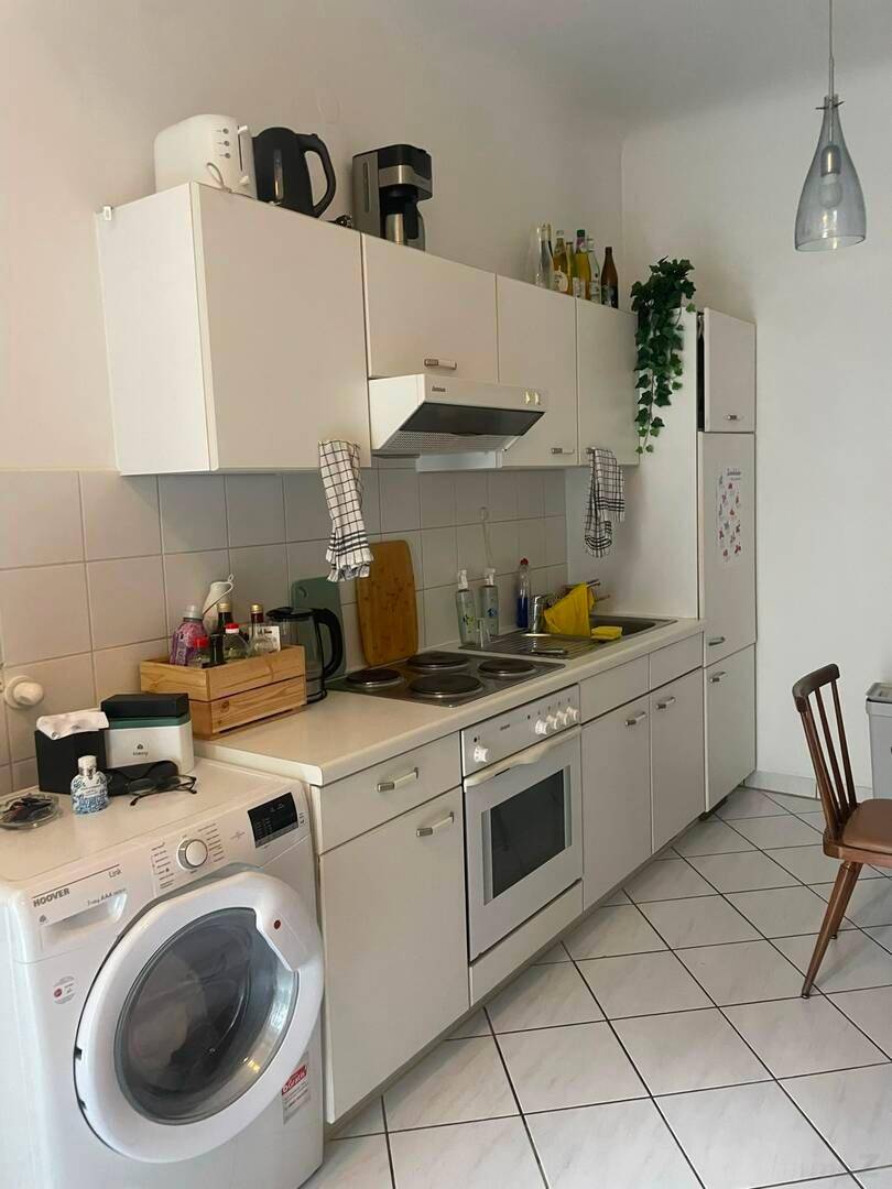 Helle Küche mit weißen Schränken, Elektroherd und Waschmaschine.