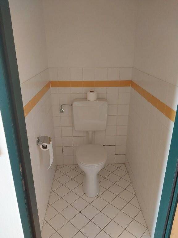 Separates WC mit Toilette und weißen Fliesen, akzentuiert durch einen gelben Streifen an der Wand.
