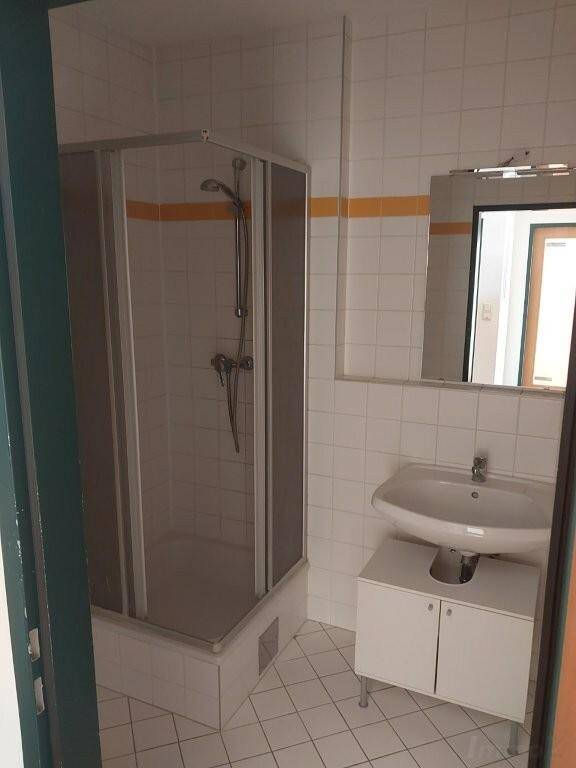 Badezimmer mit Duschkabine, Waschbecken und weißen Fliesen, akzentuiert durch einen gelben Streifen.