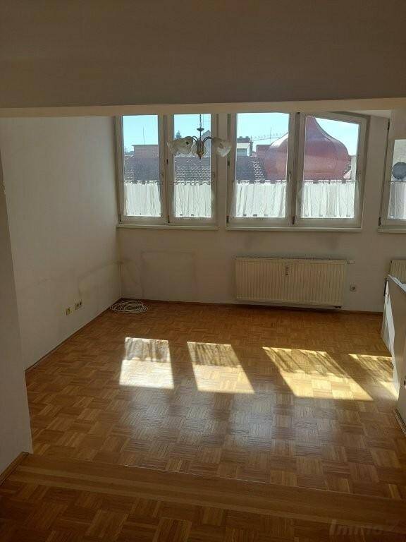 Heller Wohnraum mit Parkettboden und großen Fenstern, die viel Sonnenlicht hereinlassen.