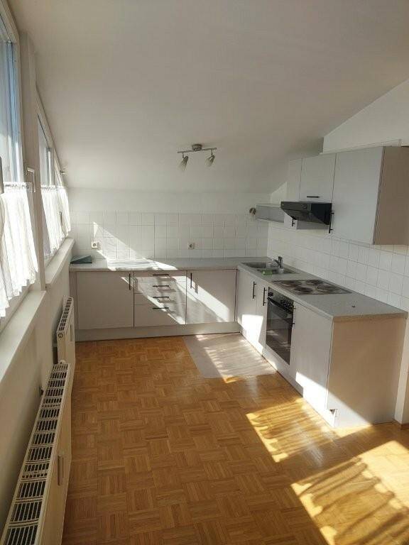 Helle Einbauküche mit weißen Schränken, Fliesenrückwand und Parkettboden, gut beleuchtet.