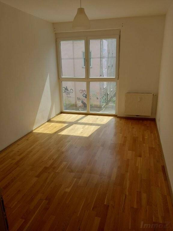 Helles Zimmer mit Parkettboden und großem Fenster zum Innenhof.