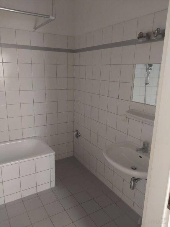 Einfaches Badezimmer mit Waschbecken, Spiegel und weißen Wandfliesen, passend zum Gesamtbild.