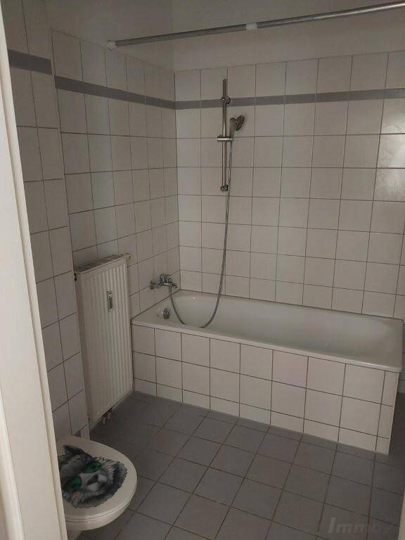 Gefliestes Badezimmer mit Badewanne und Duschvorrichtung sowie einem WC mit lustigem Deckel.