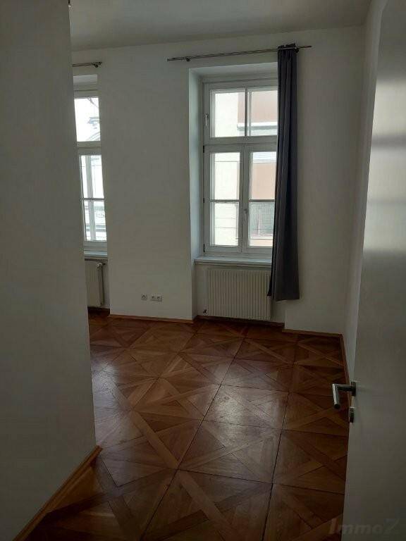 Heller Raum mit kunstvollem Parkettboden und hohen Fenstern, ideal als Wohn- oder Schlafzimmer.
