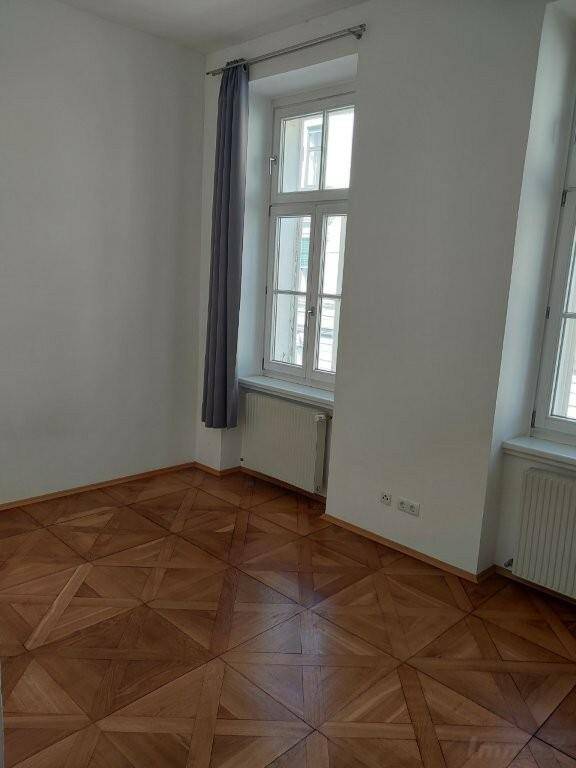 Geräumiger Raum mit elegantem Parkettboden und großen Fenstern, bietet viel Tageslicht.