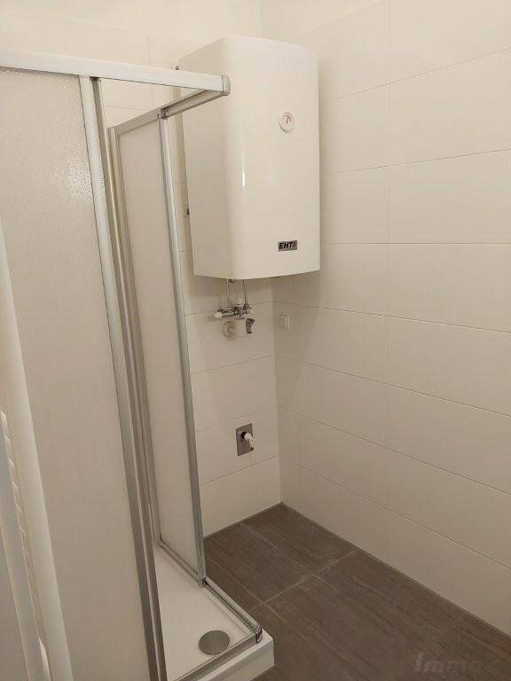 Modernes Badezimmer mit Duschkabine, Wandfliesen und Warmwasserboiler.