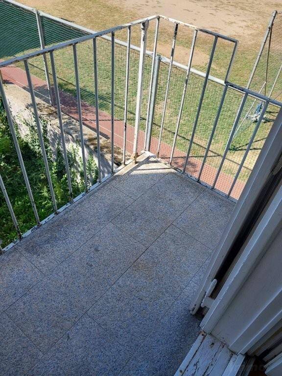 Kleiner Balkon mit Metallgeländer und Blick auf eine grüne Sportanlage.
