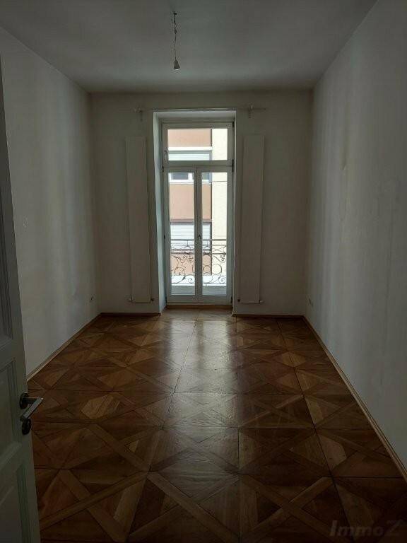 Zimmer mit klassischem Parkettboden und französischem Balkon, der für frische Luft sorgt.