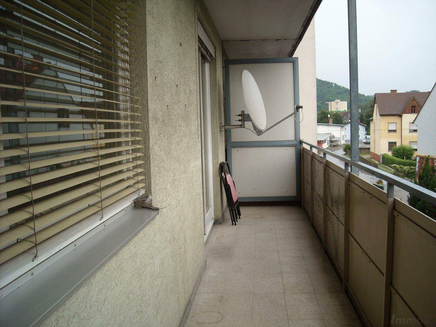 Schmaler Balkon mit Fliesenboden, Jalousien am Fenster und einer Satellitenschüssel.