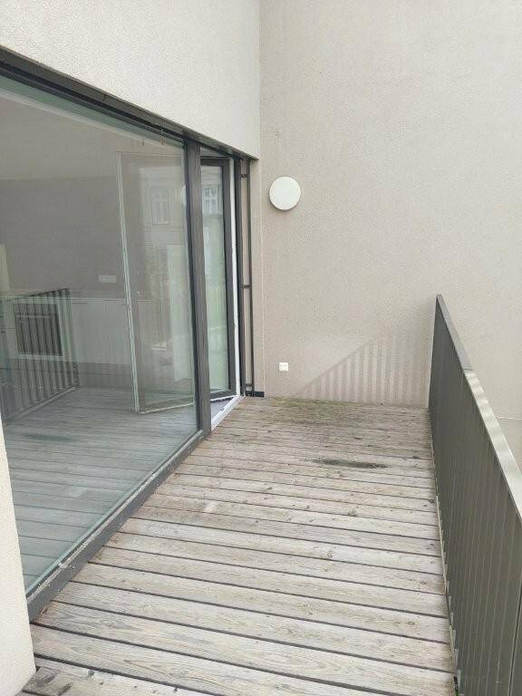 Ein Balkon mit Holzfußboden und einer Metallbrüstung, der Zugang zu einem hellen Innenraum bietet.
