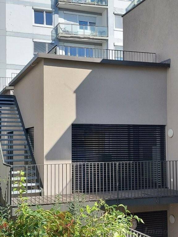 Moderne Gebäudefassade mit Außenjalousien und einer Metalltreppe, die zu einem oberen Bereich führt.