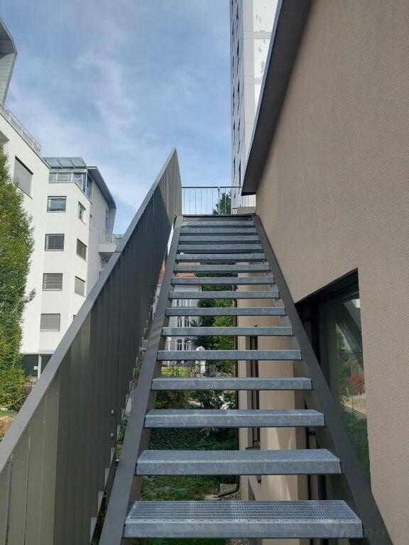 Eine moderne Außentreppe aus Metall, die zu den oberen Etagen eines Wohngebäudes führt.