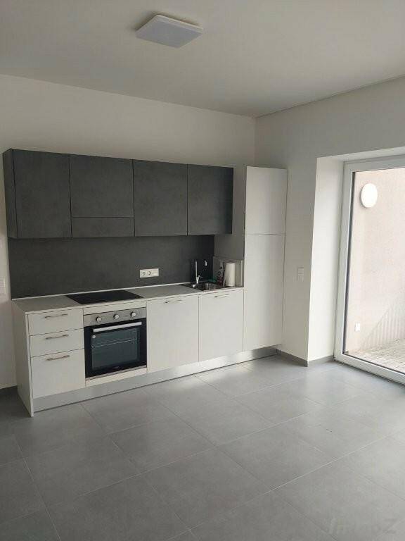 Eine moderne Einbauküche mit weißen und grauen Schränken, integriertem Backofen und Fliesenboden.