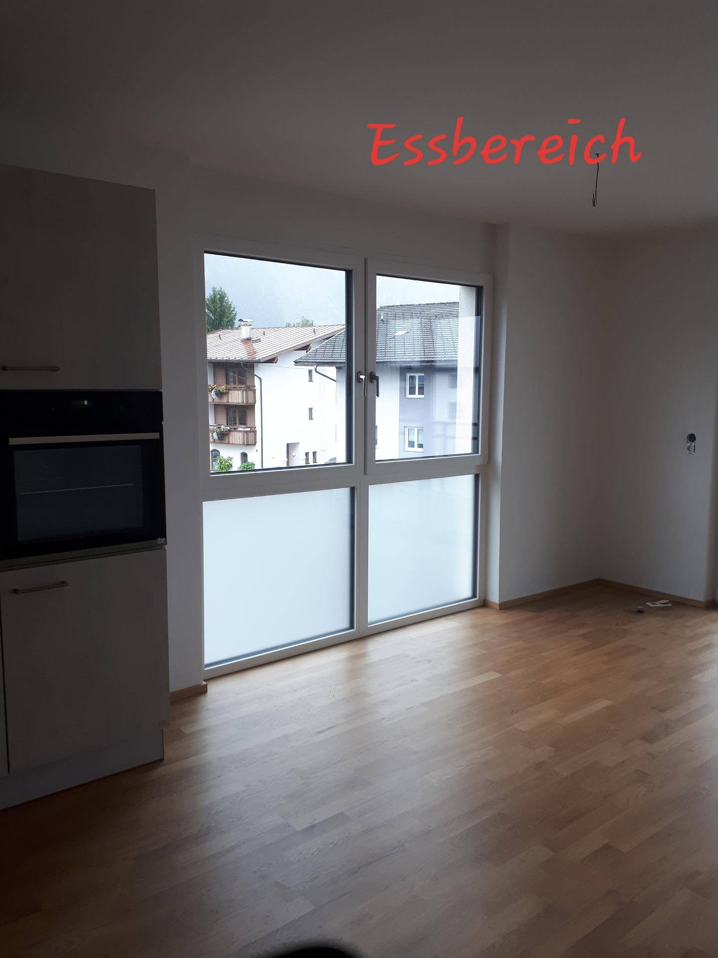 Heller Essbereich mit Holzparkettboden und großem Fenster, angrenzend an die moderne Küche.