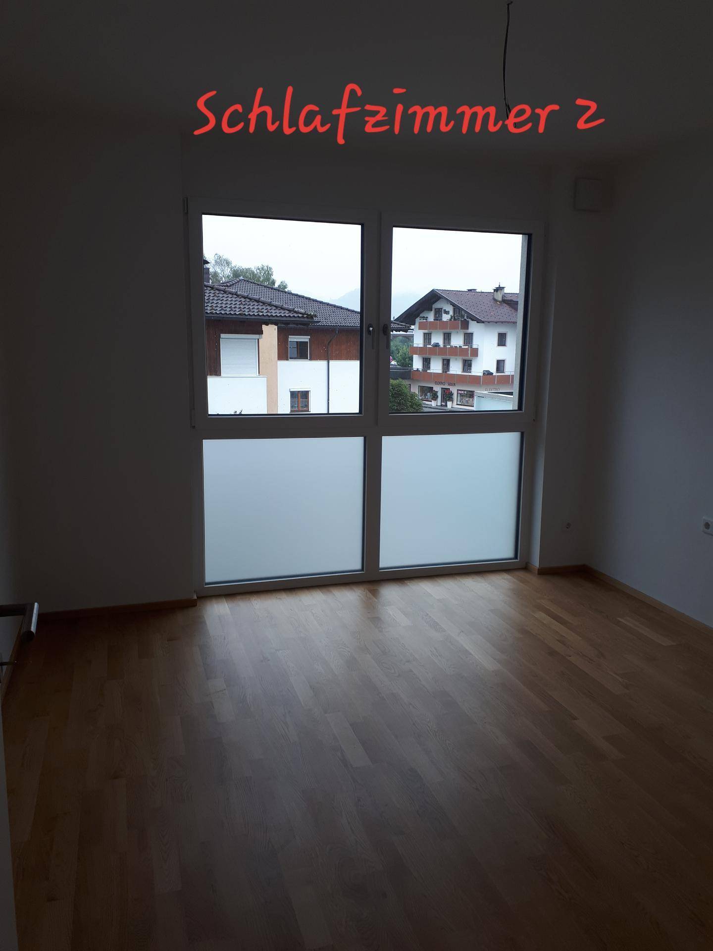 Geräumiges Schlafzimmer mit hellem Holzfußboden und Fensterfront, die den Blick auf die Nachbarschaft freigibt.