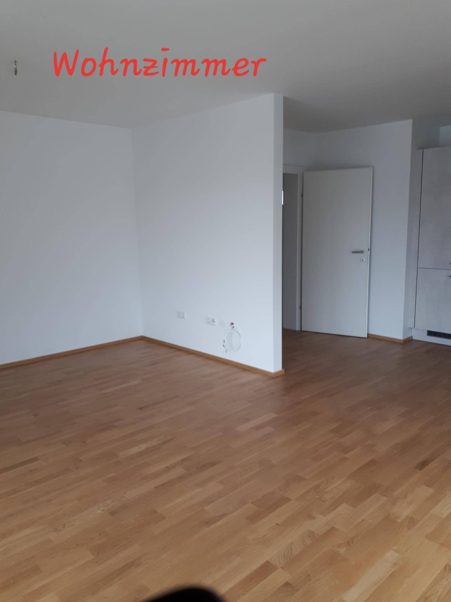 Geräumiges Wohnzimmer mit hellem Holzfußboden und weißen Wänden, bereit für individuelle Gestaltung.
