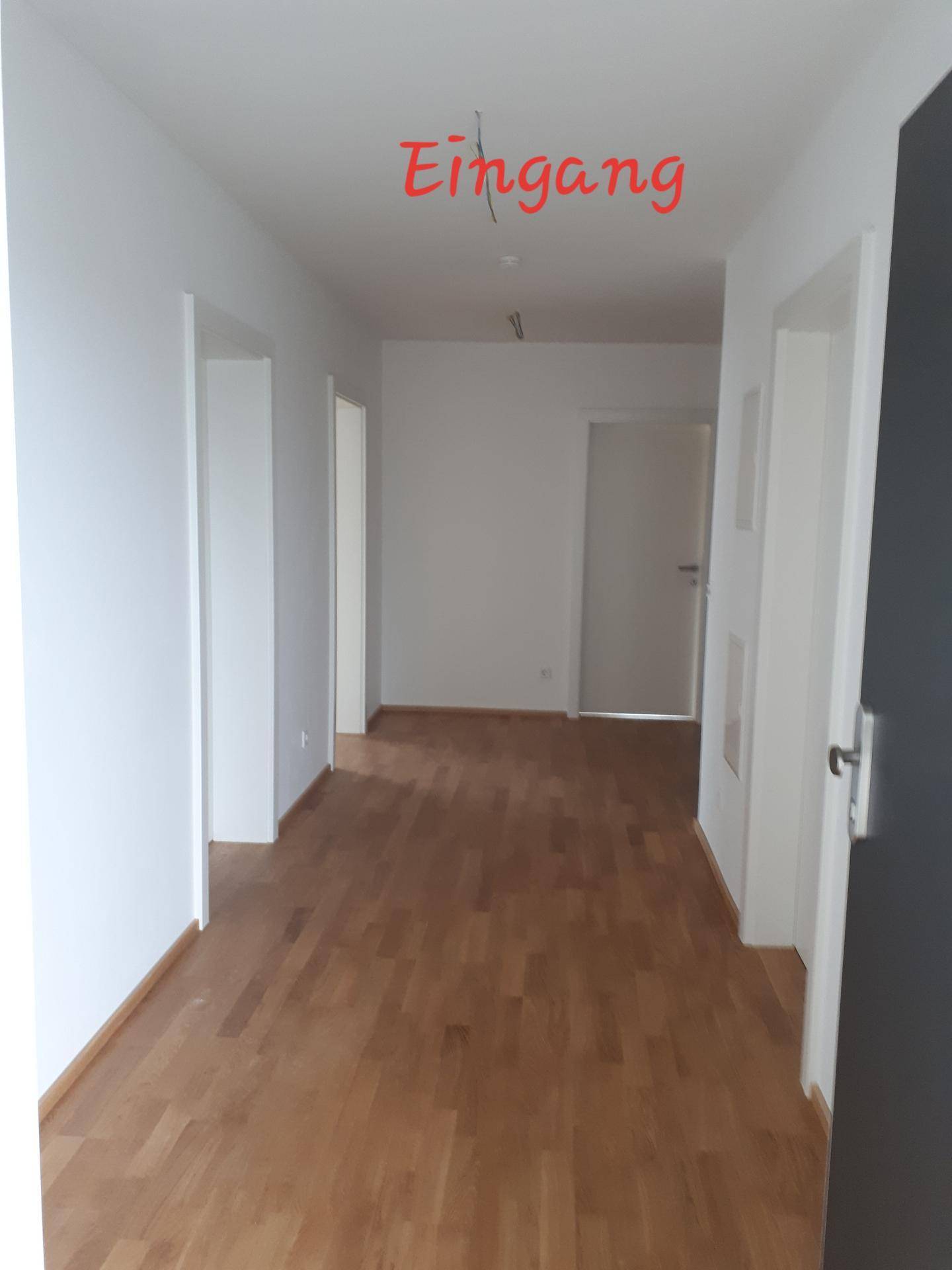 Heller Eingangsbereich mit Holzparkettboden und weißen Wänden, der zu verschiedenen Räumen führt.