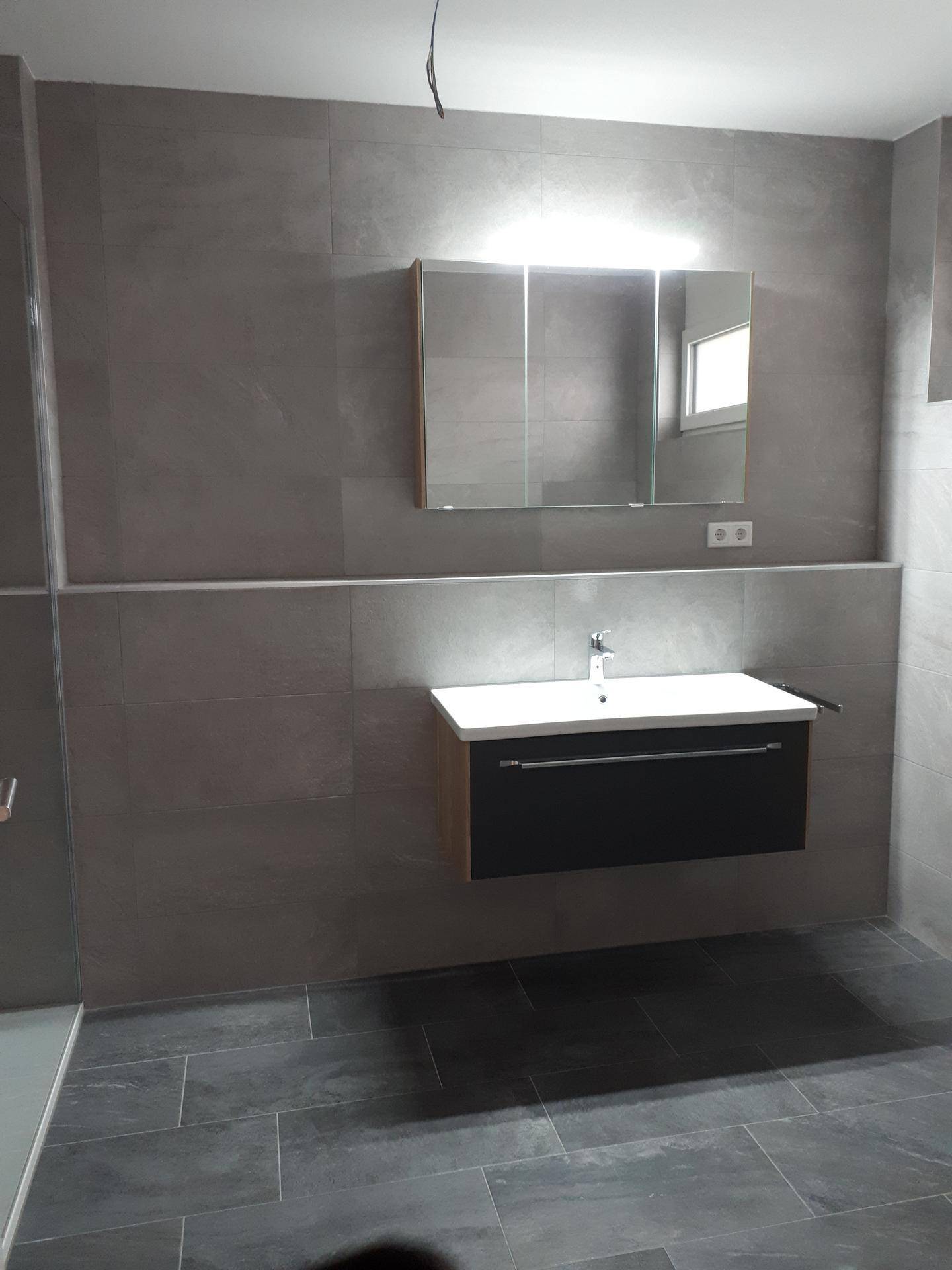 Modernes Badezimmer mit grauen Fliesen, schwebendem Waschtisch und Spiegelschrank über dem Waschbecken.