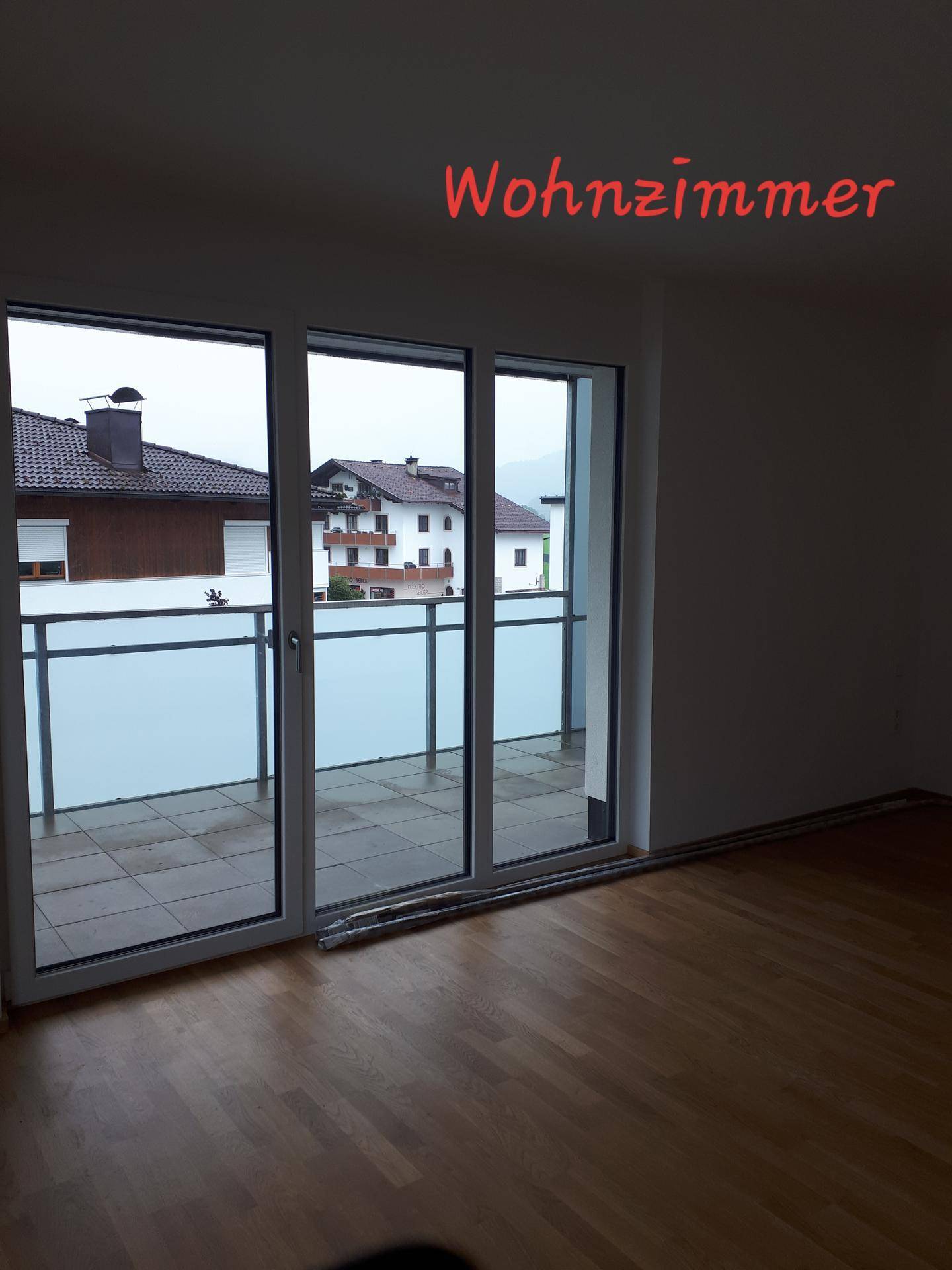 Lichtdurchflutetes Wohnzimmer mit Holzparkettboden und direktem Zugang zu einem Balkon durch eine große Schiebetür.