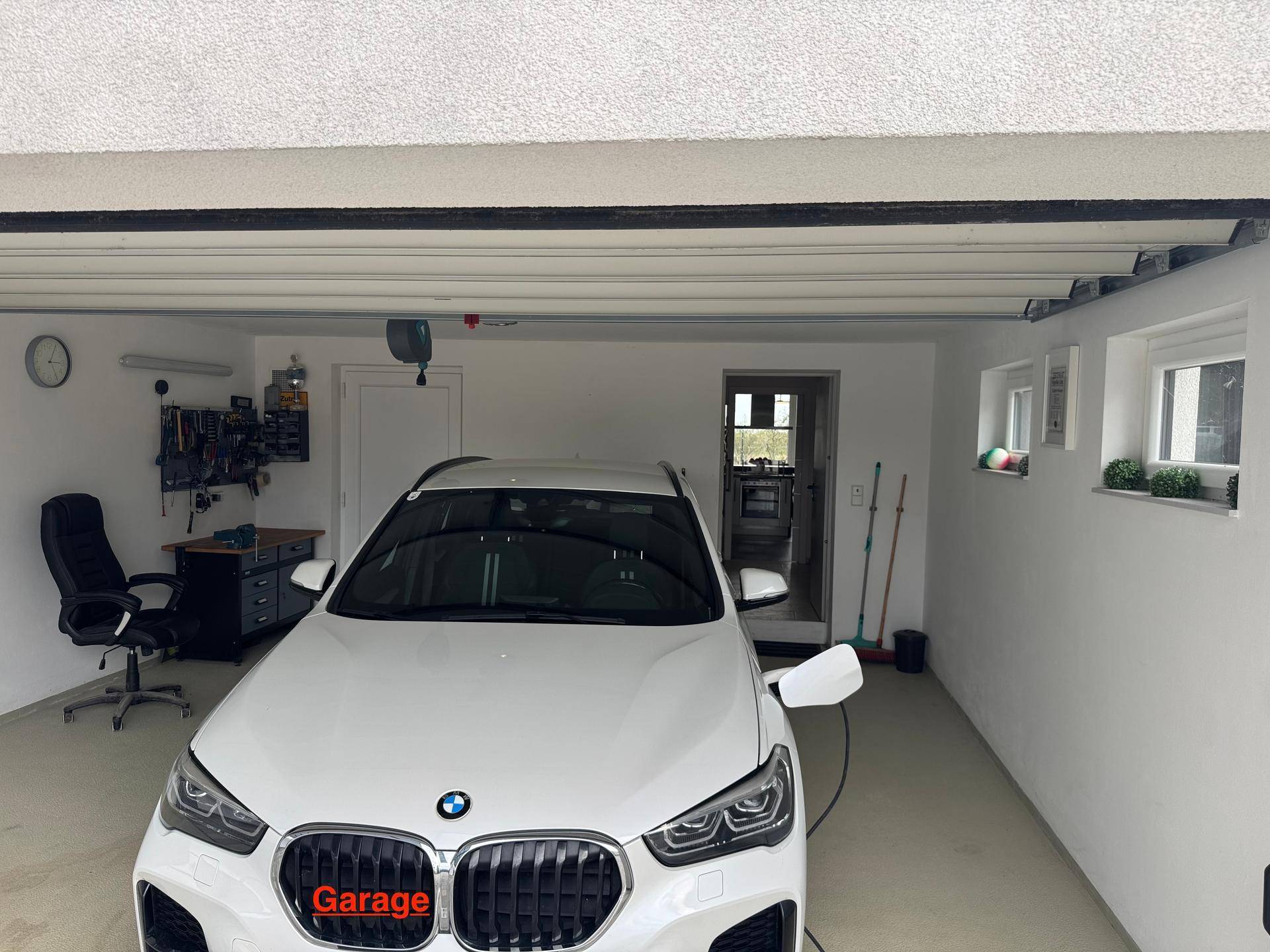 Geräumige Garage mit Werkbank, Werkzeugwand und einem geparkten Auto.