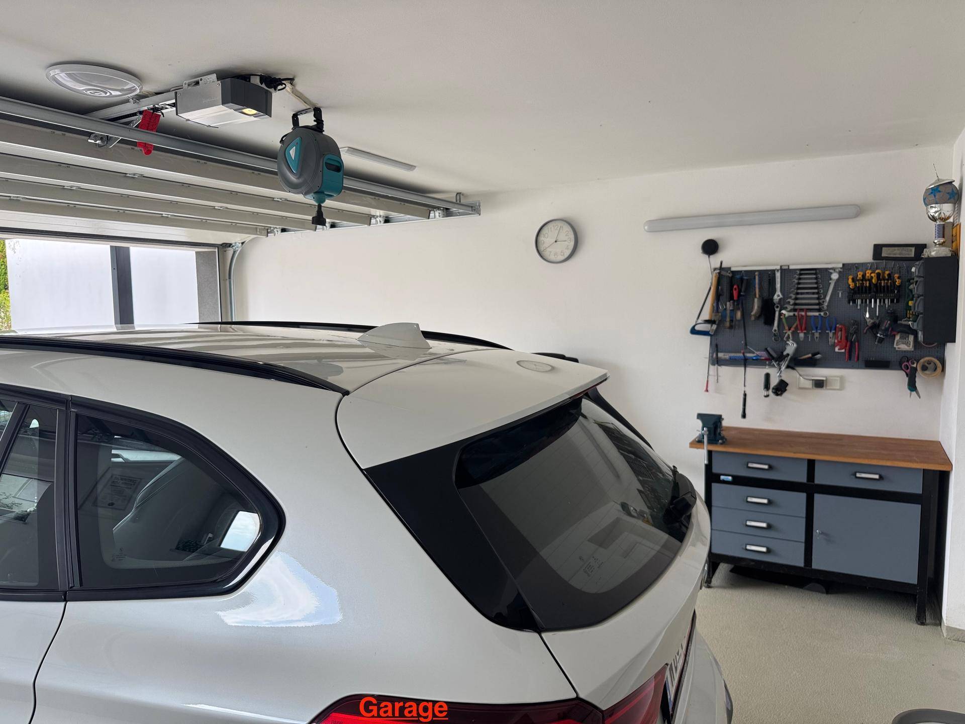 Gut ausgestattete Garage mit Werkbank, Werkzeugwand und automatischem Garagentor.
