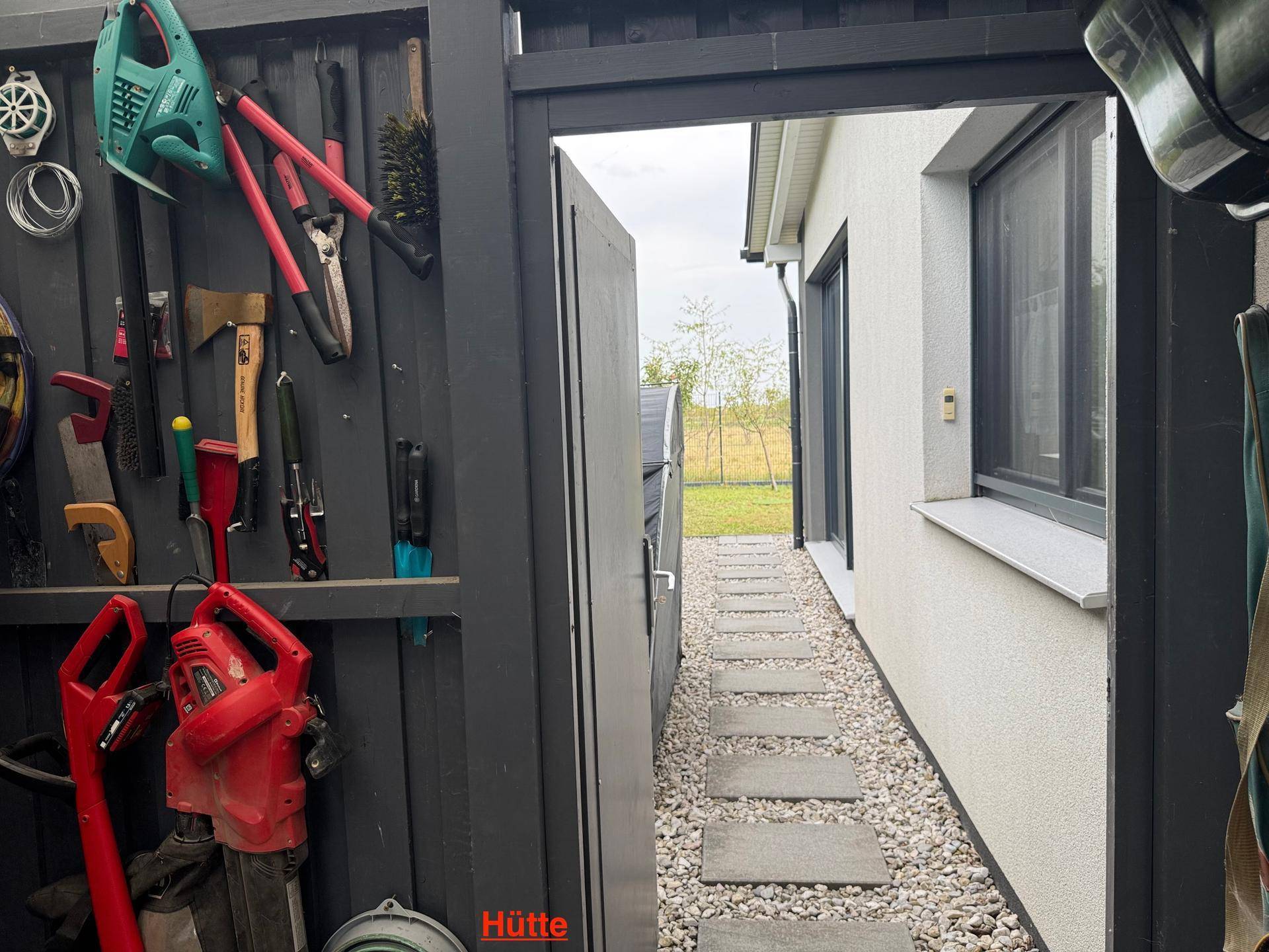 Schmaler Zugangsweg zum Gartenbereich neben dem Haus mit Blick auf eine Werkzeugwand.