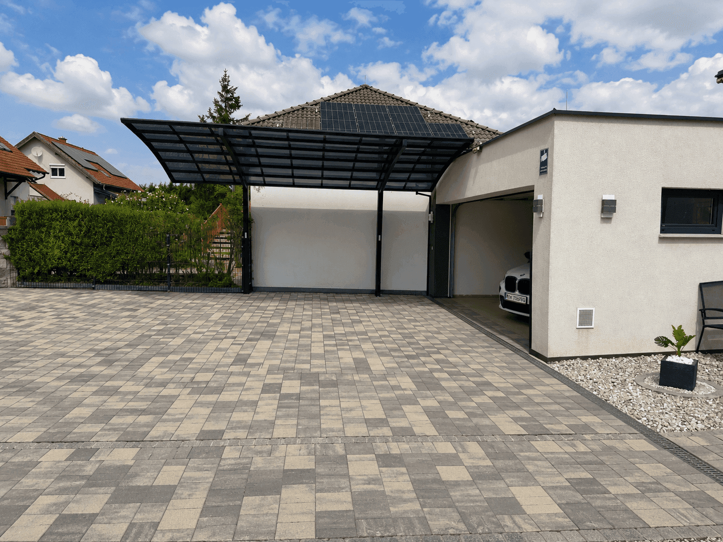 Überdachter Carport und Garage mit gepflasterter Zufahrt und Solarpaneelen auf dem Dach.