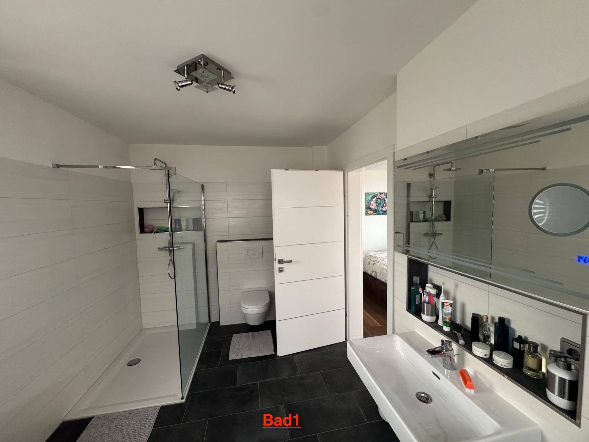 Helles Badezimmer mit großem Waschbecken, Spiegel und begehbarer Dusche mit Glasabtrennung.