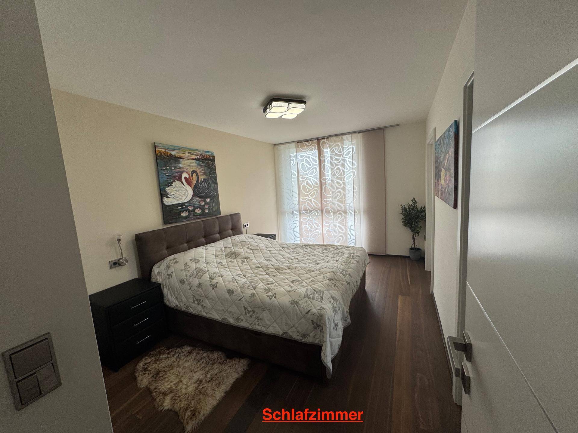 Gemütliches Schlafzimmer mit Doppelbett, Holzboden und großen Fenstern für viel Tageslicht.