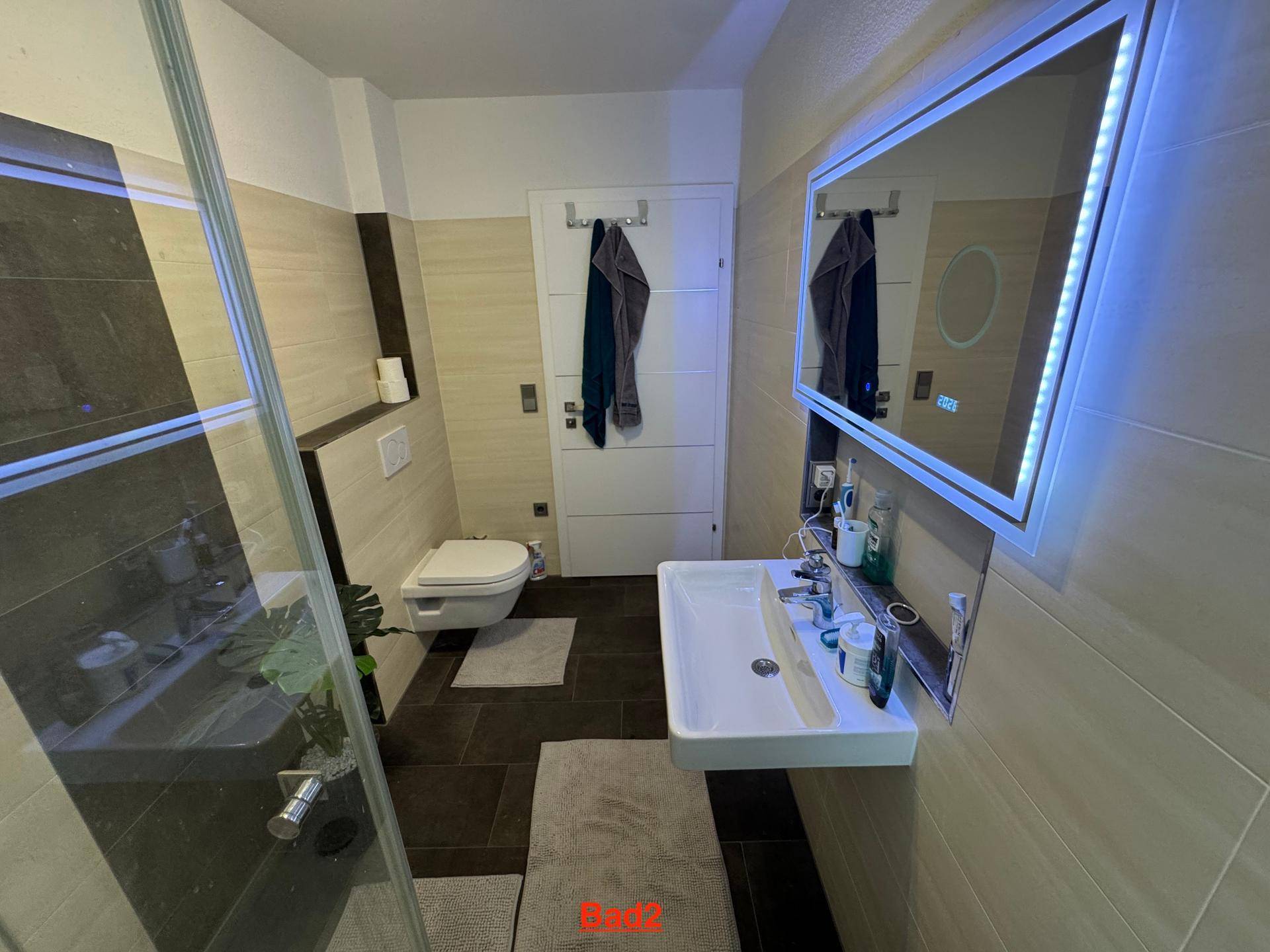 Modernes Badezimmer mit Dusche, wandhängendem WC und beleuchtetem Spiegelschrank.