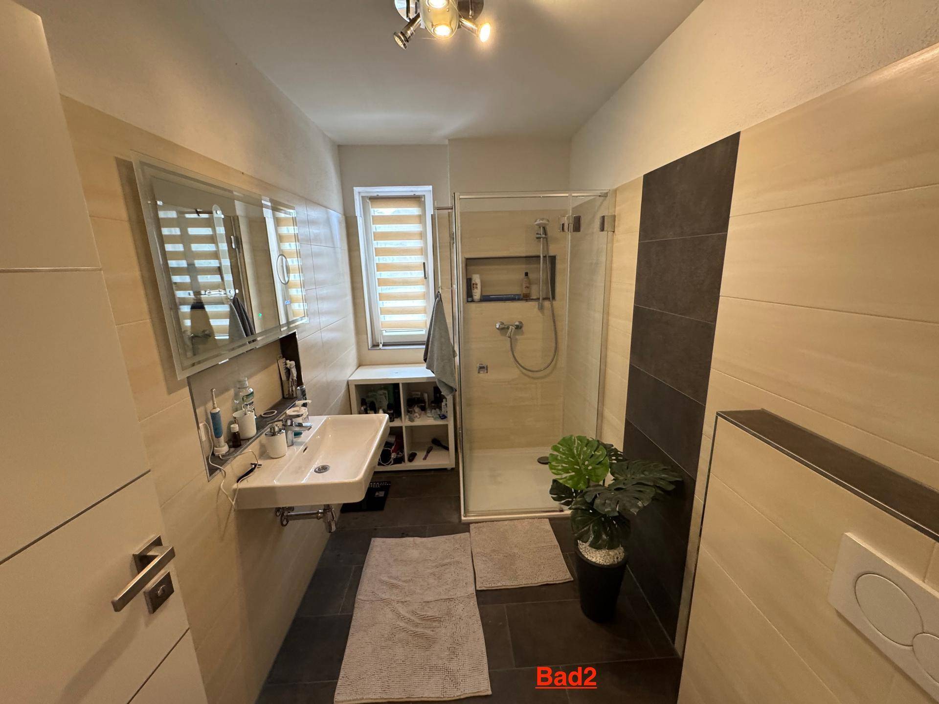 Helles Badezimmer mit Dusche, Waschtisch und Fenster für natürliche Belüftung.