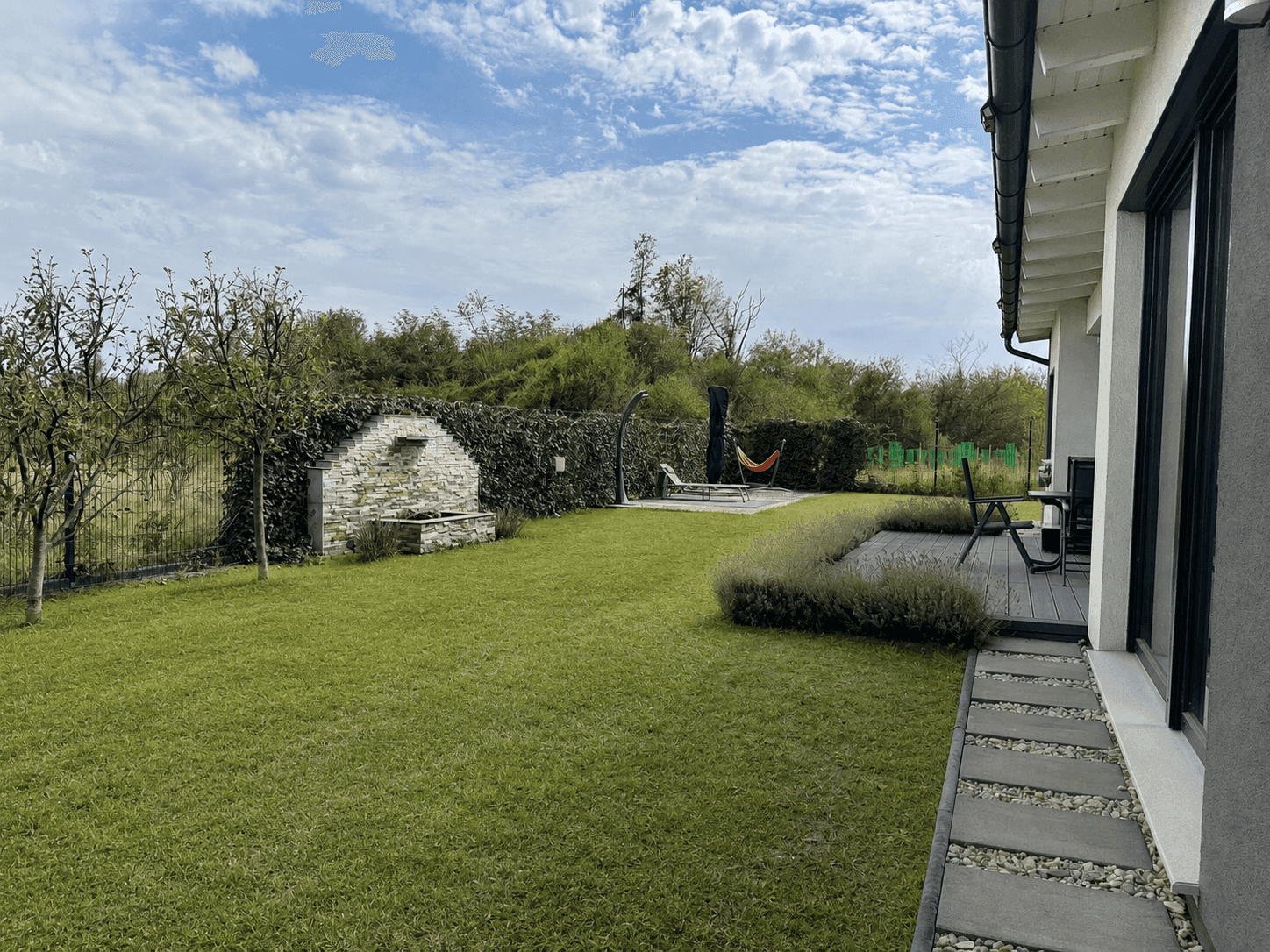 Grüner Gartenbereich mit Liegefläche, Hängematte und Außendusche, umgeben von üppigem Grün.