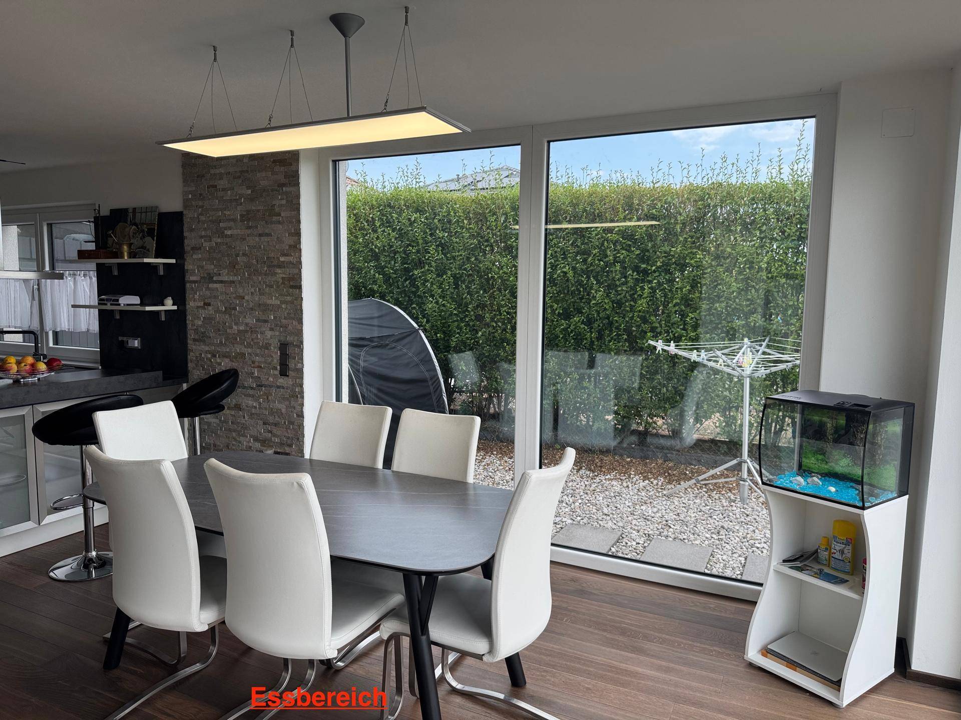 Heller Essbereich mit großem Tisch, modernen Stühlen und weitem Blick in den Garten.