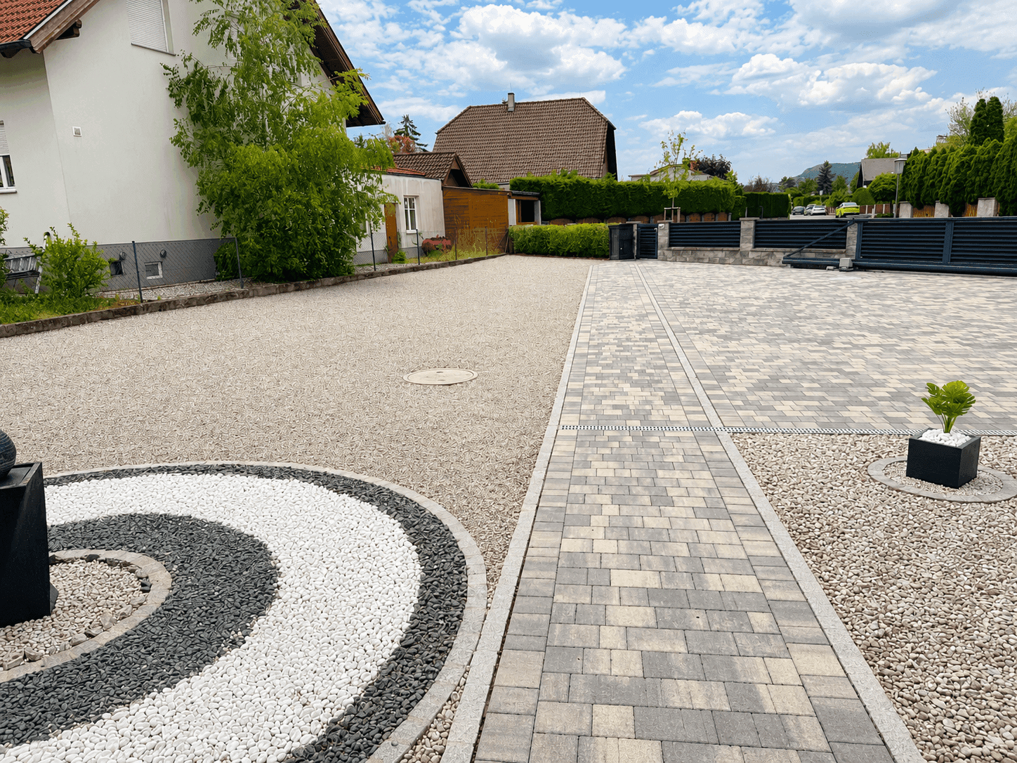 Weitläufige Auffahrt mit gepflastertem Weg und Kiesflächen, umgeben von Hecken und Bäumen.
