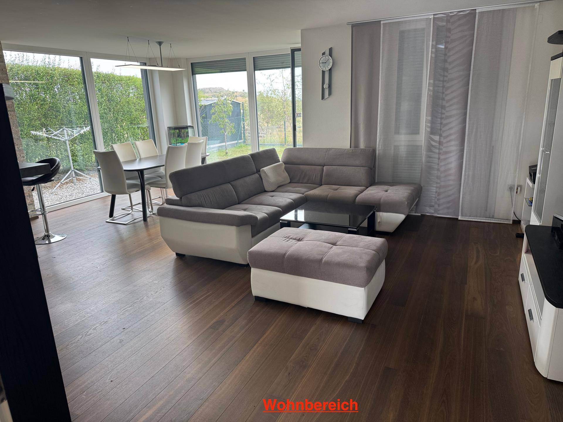 Geräumiger Wohnbereich mit bequemer Eckcouch, Holzboden und großen Fenstern zum Garten.
