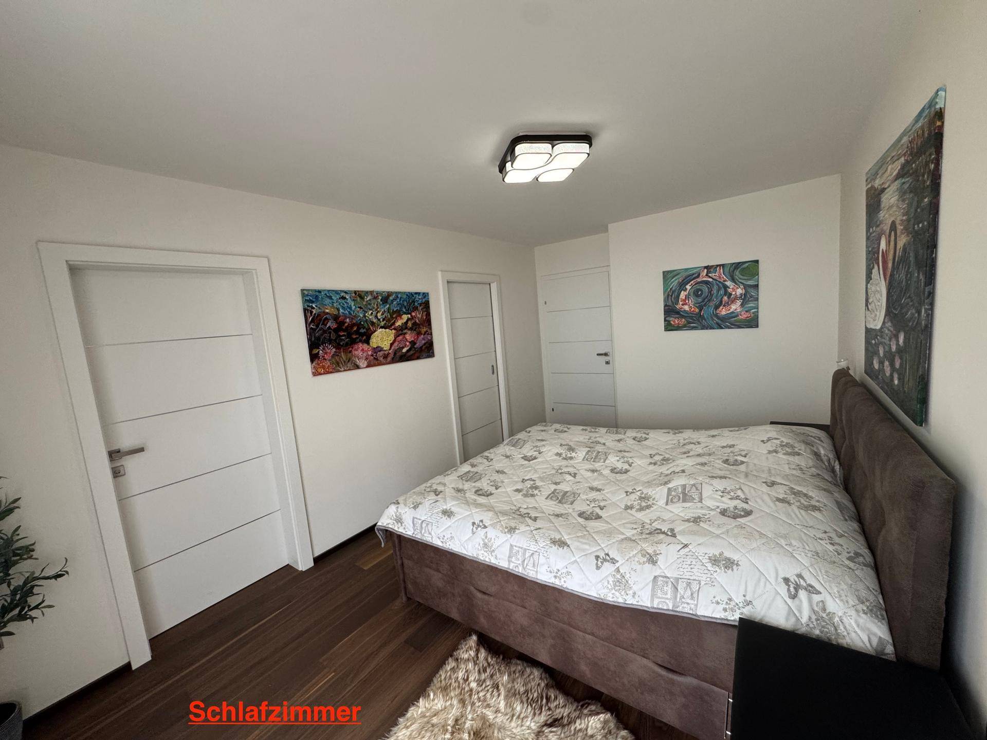 Helles Schlafzimmer mit modernem Doppelbett, Holzboden und weißen Türen zu angrenzenden Räumen.