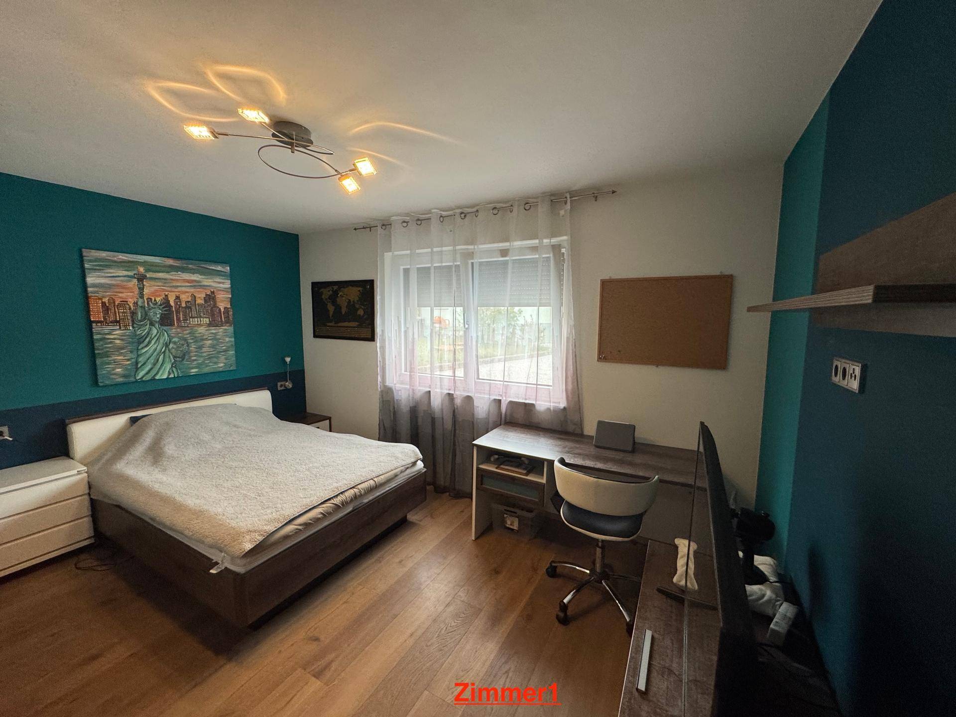 Schlafzimmer mit Holzboden, farbiger Wandgestaltung und einem Schreibtischbereich.