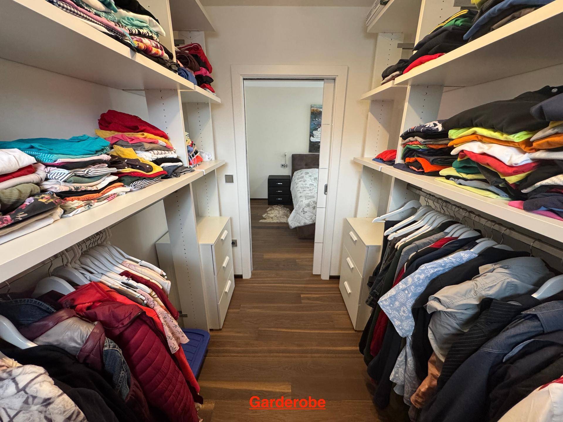 Geräumiger begehbarer Kleiderschrank mit viel Stauraum und Blick ins Schlafzimmer.