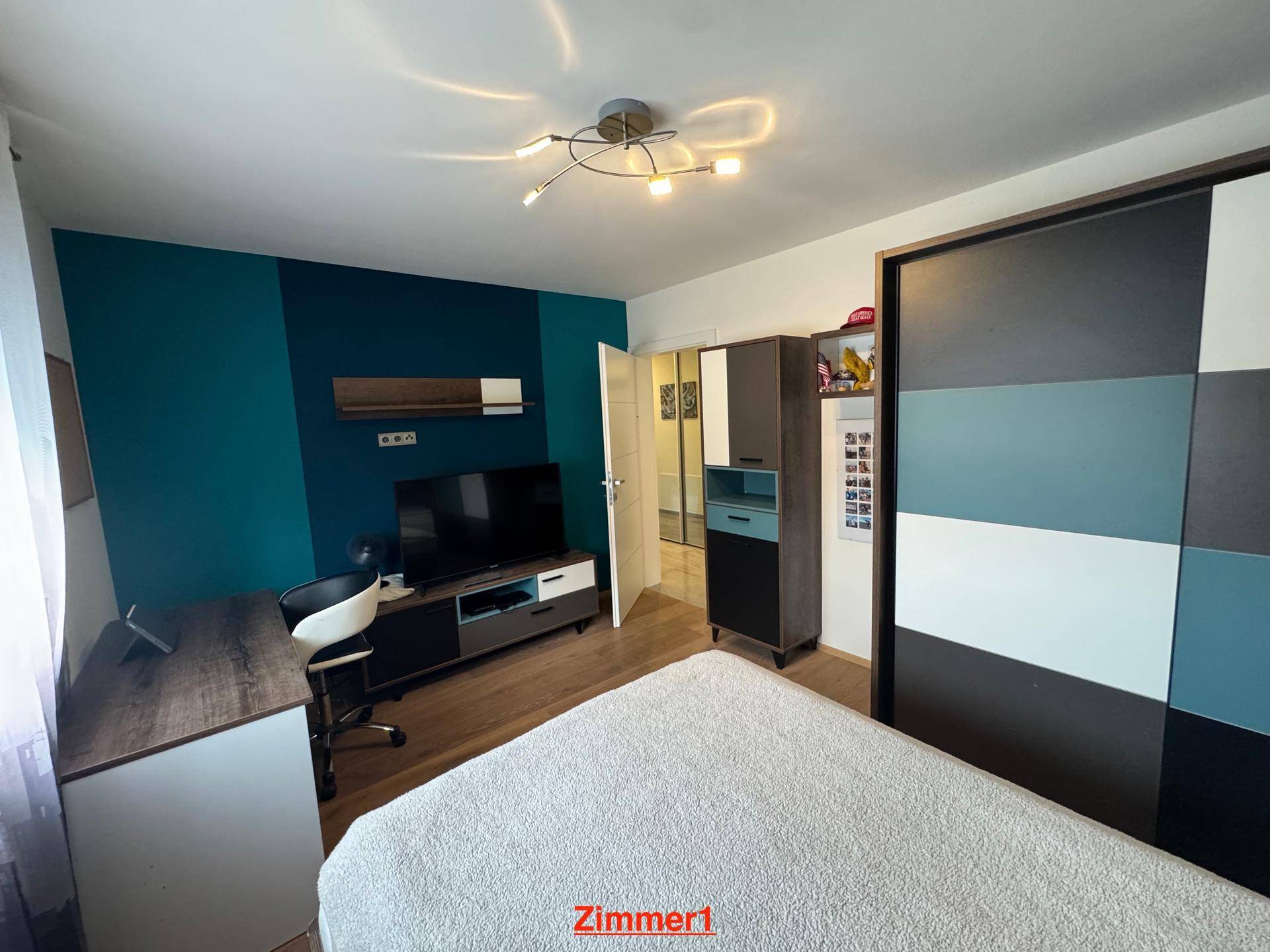 Modern eingerichtetes Schlafzimmer mit Holzboden, Schiebetürenschrank und farbiger Akzentwand.