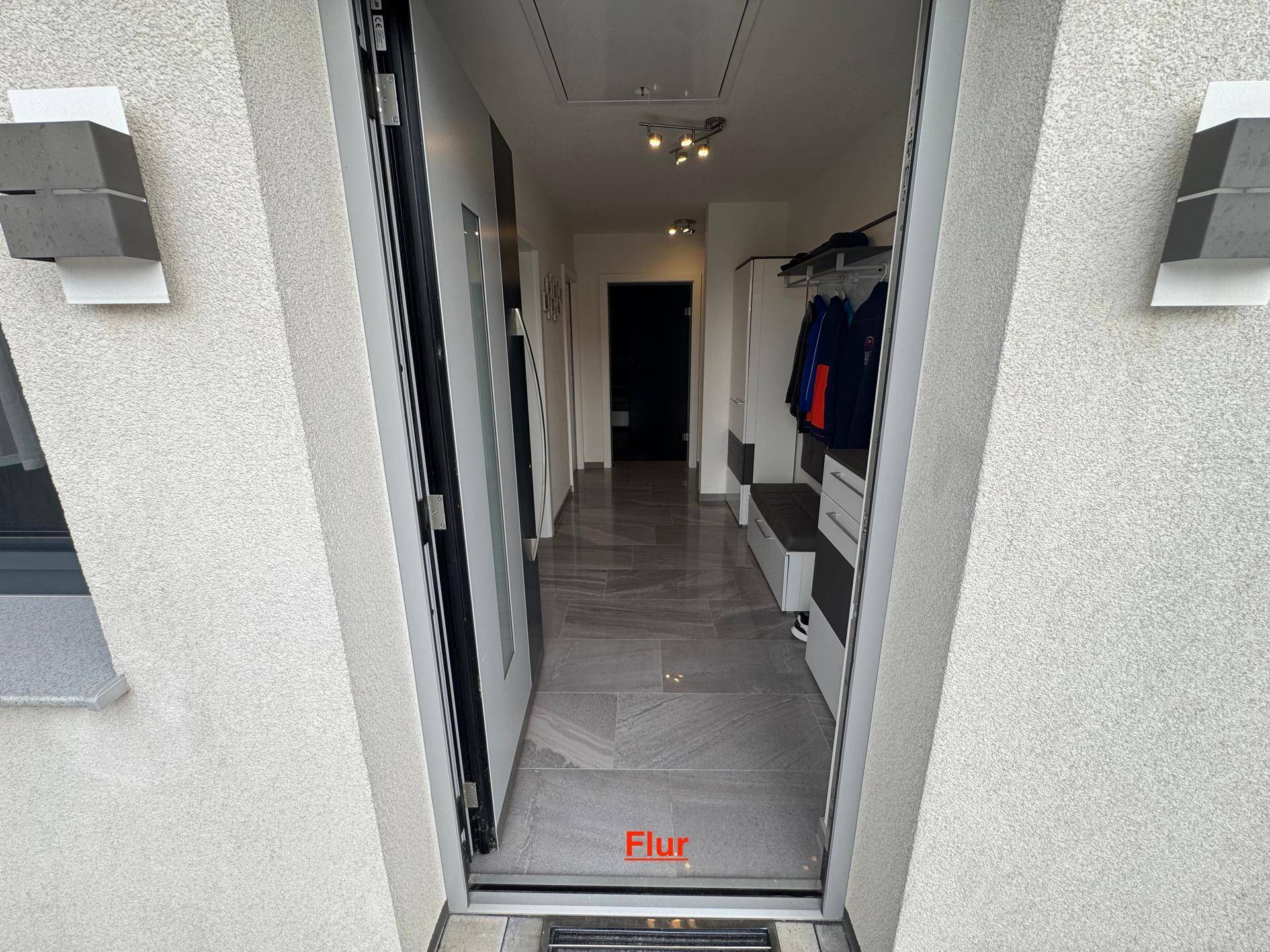 Heller Eingangsbereich mit modernen Fliesen, Garderobe und Blick in den weiteren Flur.