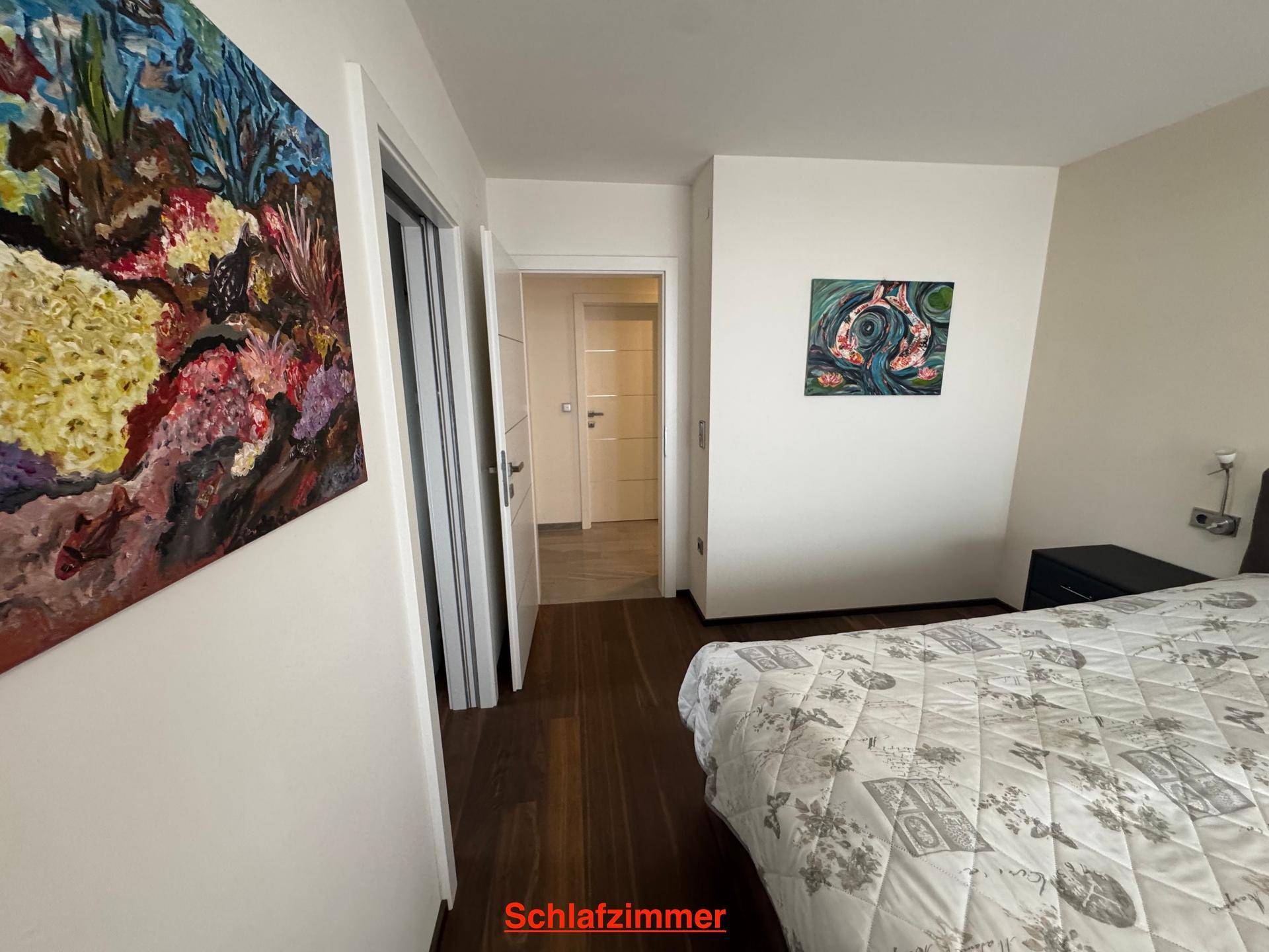 Schlafzimmer mit Holzboden und Blick auf den Flur, ausgestattet mit modernen Kunstwerken.